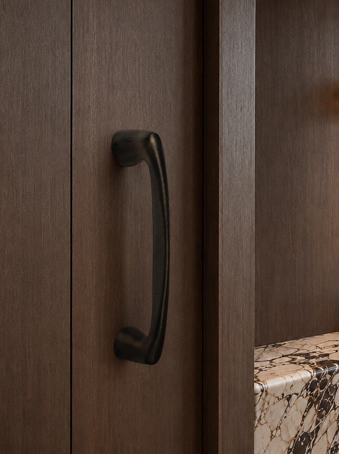 Close-up of a dark cabinet handle on a wooden cabinet with a marble countertop.